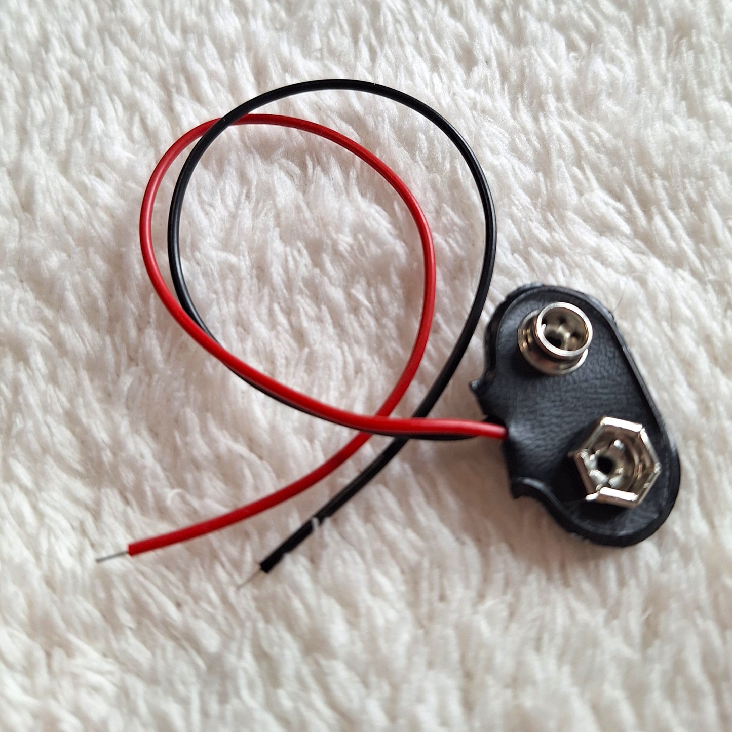 close up view of a black 9v battery connector, connected to approx 10cm of thin clack and red wire.