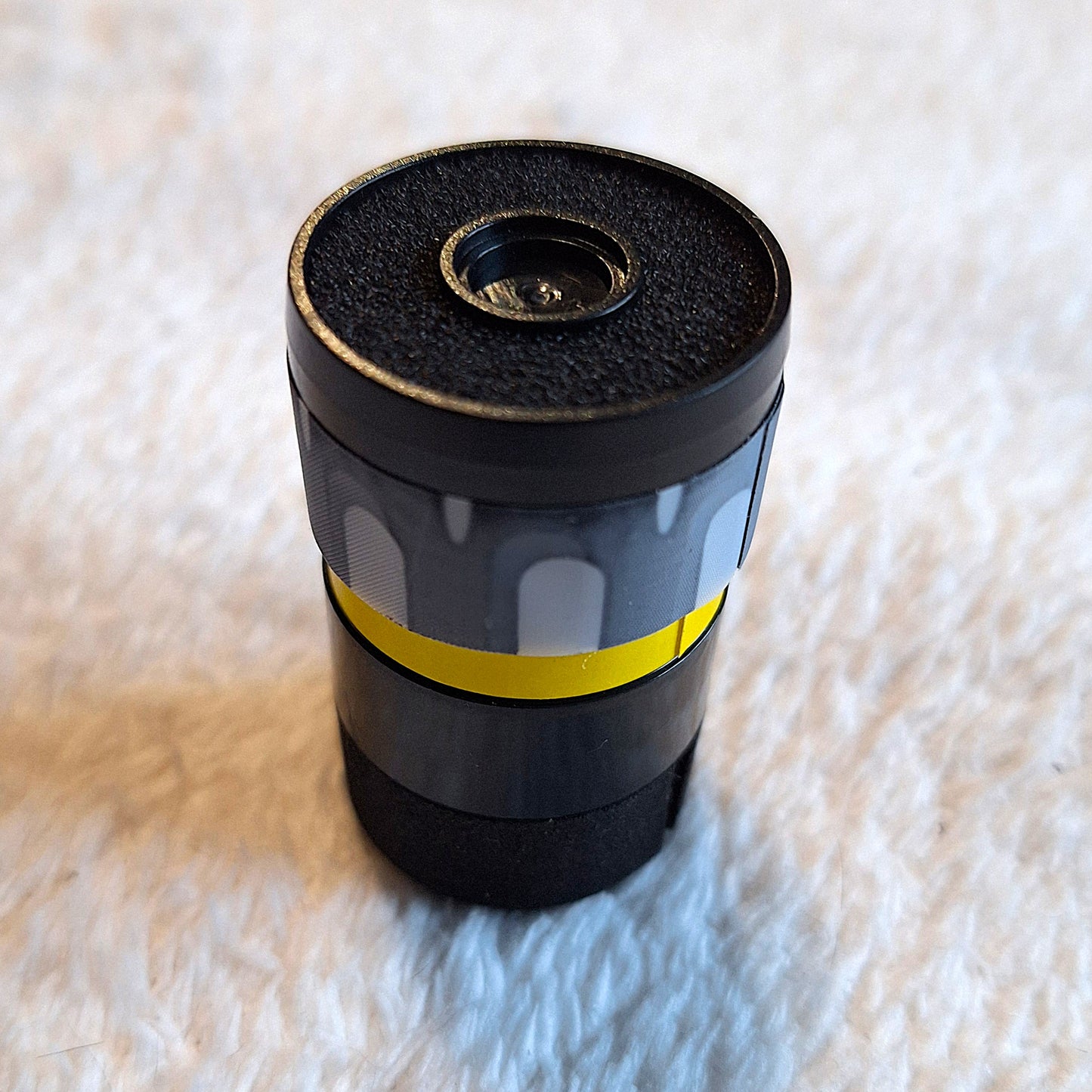 close up of a black 30mm wide microphone capsule sitting face-up on a white surface.