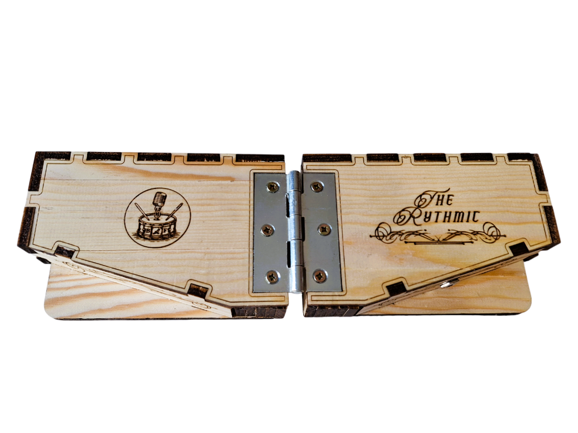 Opened front top oblique view of  'The Rhythmic' described as two laser-cut and etched pine boxes, each with a contoured bottom edge. both with a brass D-ring on the upper box edge, One box has steam-punk inspired laser etching with a rhythmic logo of a microphone on a drum, the other laser etched Victoriana script reading 'The Rhythmic'. It is hinged with a metal connector and connected discretely with 2 wires. On a transparent background
