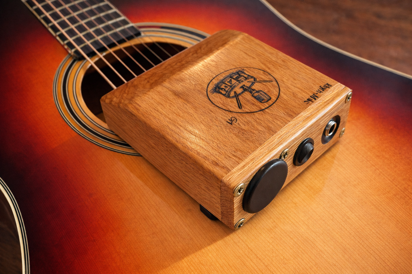 Rhyth-Mic G1 posed on an acoustic guitar, showing the on/off, battery cover and 6.3mm output jack. Rear view photo