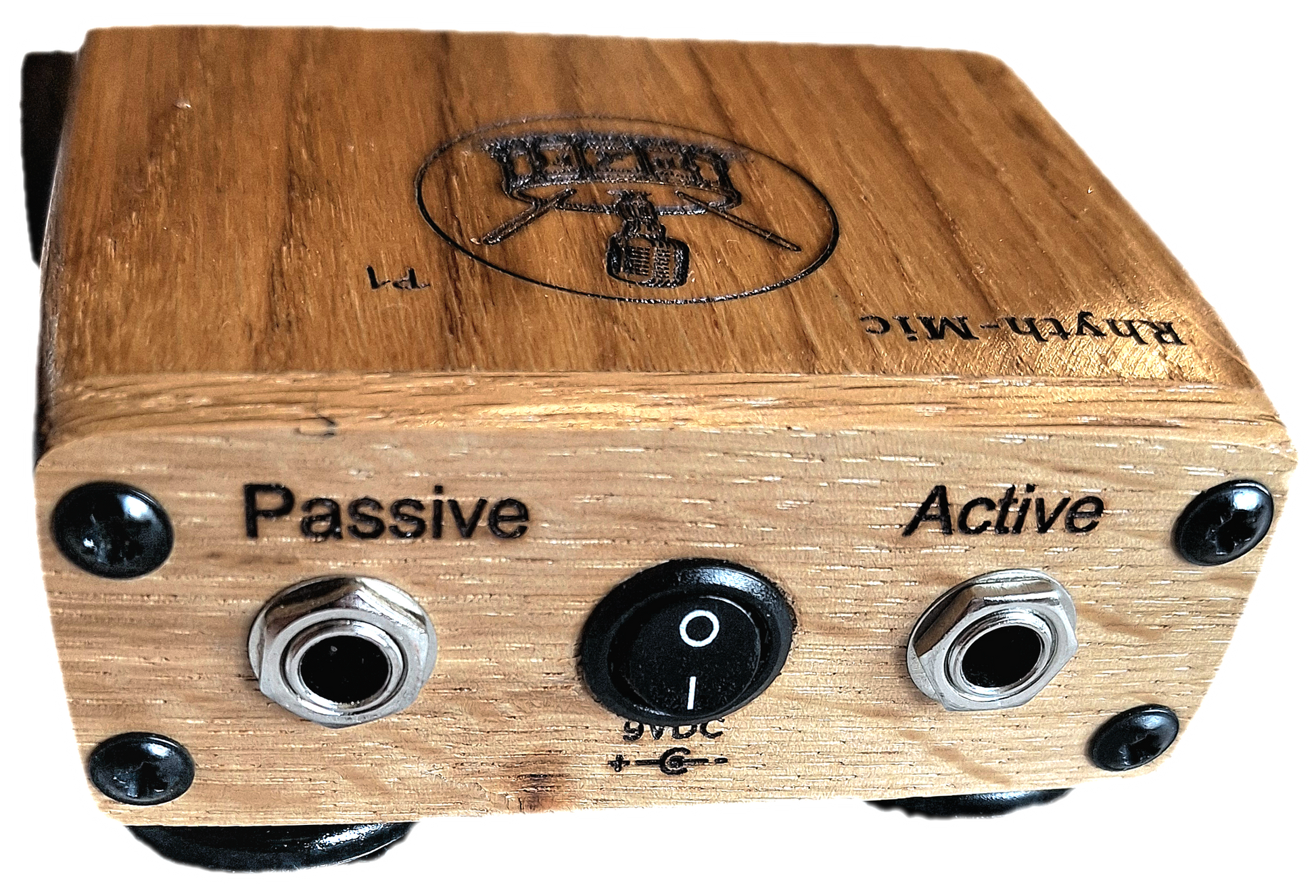 Rear close- in view of the Rhyth-mic P1 play-through stompbox in solid oak wood showing laser etched branding of a microphone on a drum plus an on off switch, and passive and active input output 1/4 " jacks