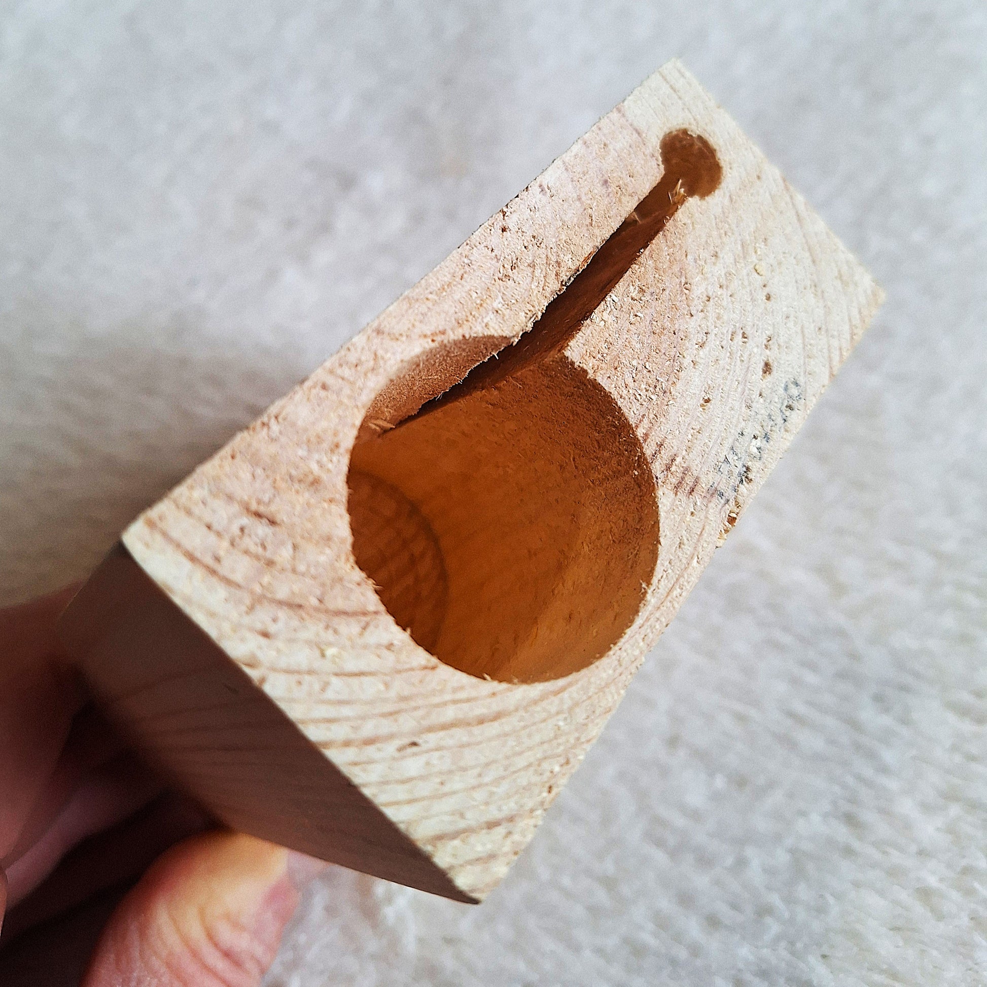 Handheld rear view of a solid pine stomp box enclosure cut to a wedge shape ready to to be used in a DIY build. On a white background.