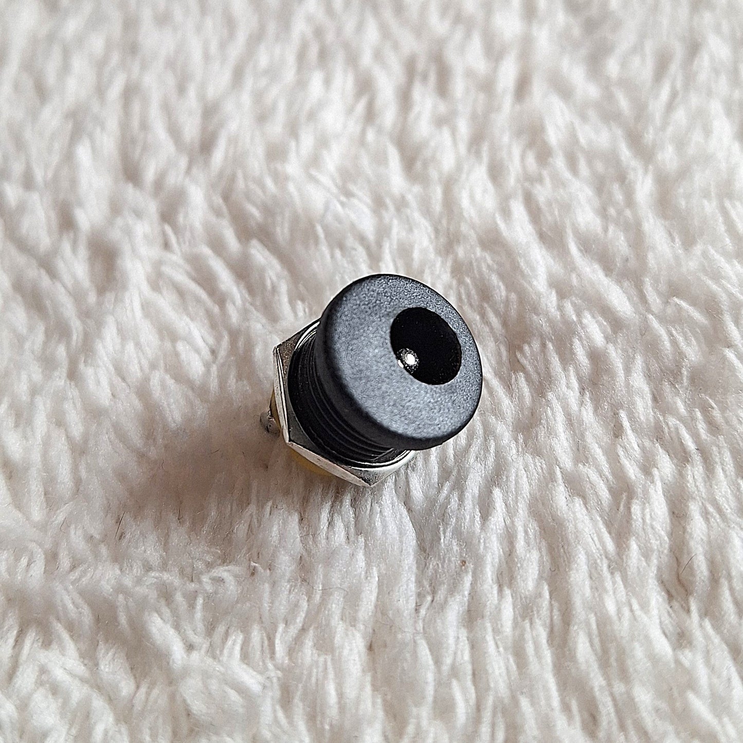 Close up of Black standard guitar effects pedal power jack, facing upwards on a white background
