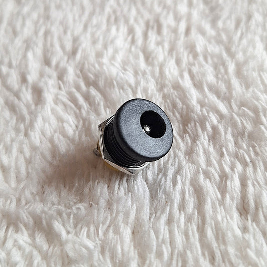 Close up of Black standard guitar effects pedal power jack, facing upwards on a white background